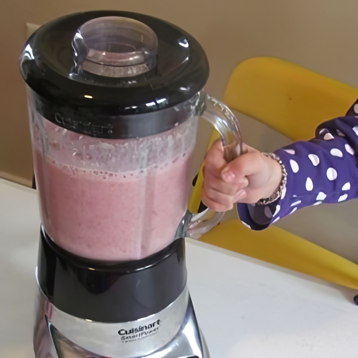 strawberry and banana smoothie on a blender with kid's hand