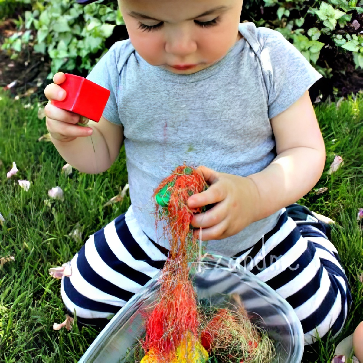 baby playing with colored silk from corn husks as sensory bins for preschoolers
