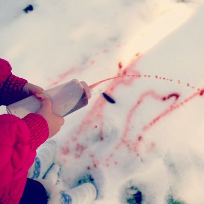 Kid spraying food coloring to draw on snow as outdoor games to burn off steam