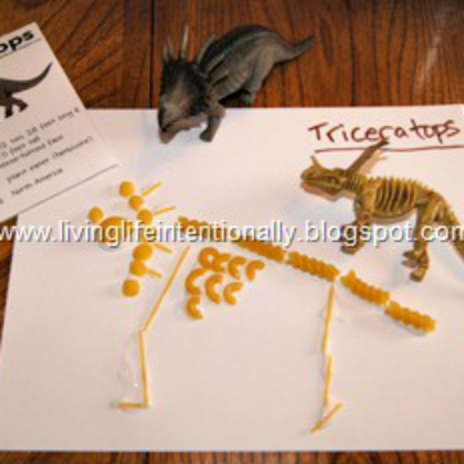 pasta dinosaur - dinosaur toys on top of paper with pasta forming a dinosaur skeleton