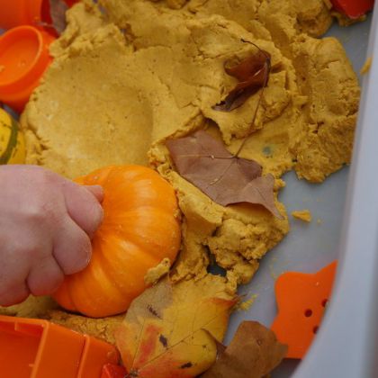 Fall Pumpkin Play Dough Bin by Wildflower Ramblings- kid's hand squishing the play dough with a pumpkin