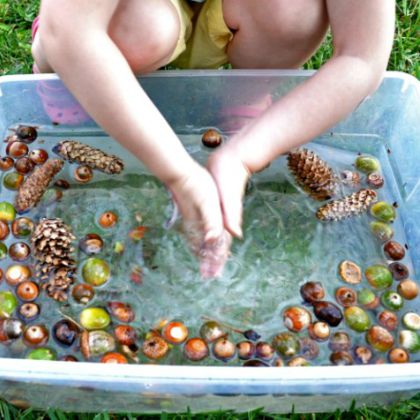 Signs of Autumn Sensory Bin (B-Inspired Mama)- Toddler playing with a fall sensory bin of water with crab apples, pine cones and acorn